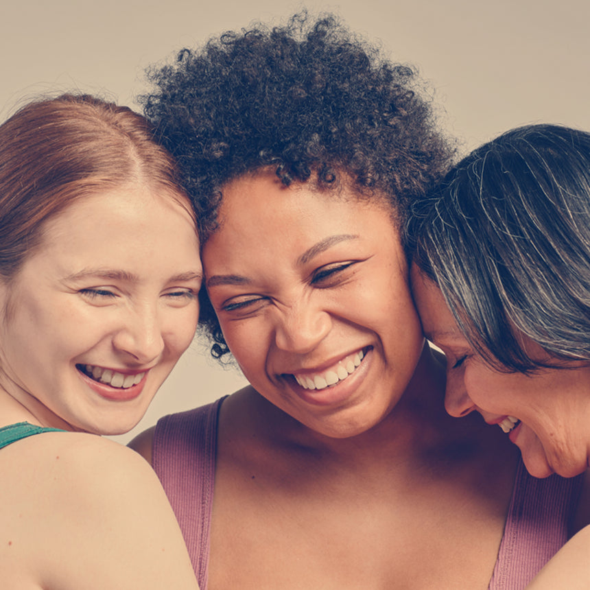 Three women laughing together with a plain background