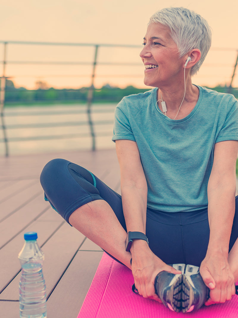 Woman stretching on a pink mat outdoors with a water bottle nearby